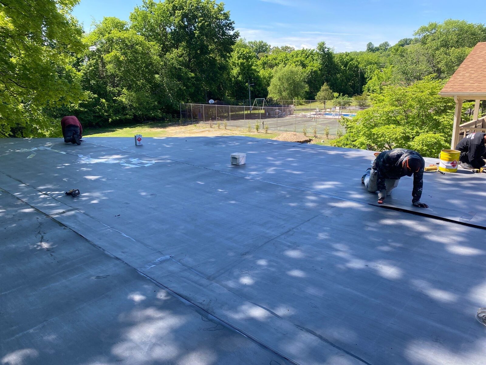 Crew installing EPDM membrane on a flat commercial roof with trees in the background