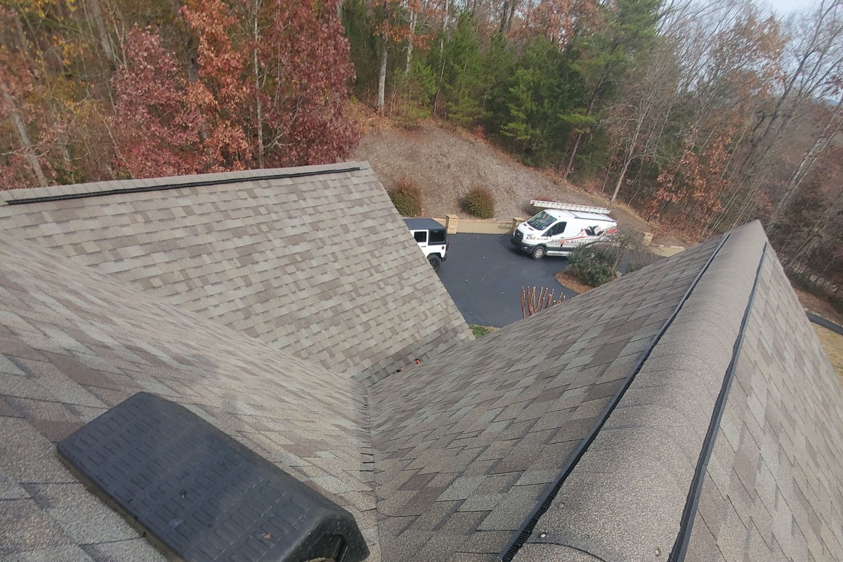 Roof valley where two shingle slopes meet, with a Brian King Roofing van parked in the driveway below